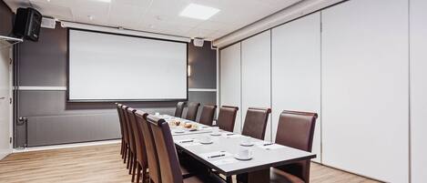 Una sala de conferencias con una mesa larga, sillas, una pantalla de proyector y una pizarra.