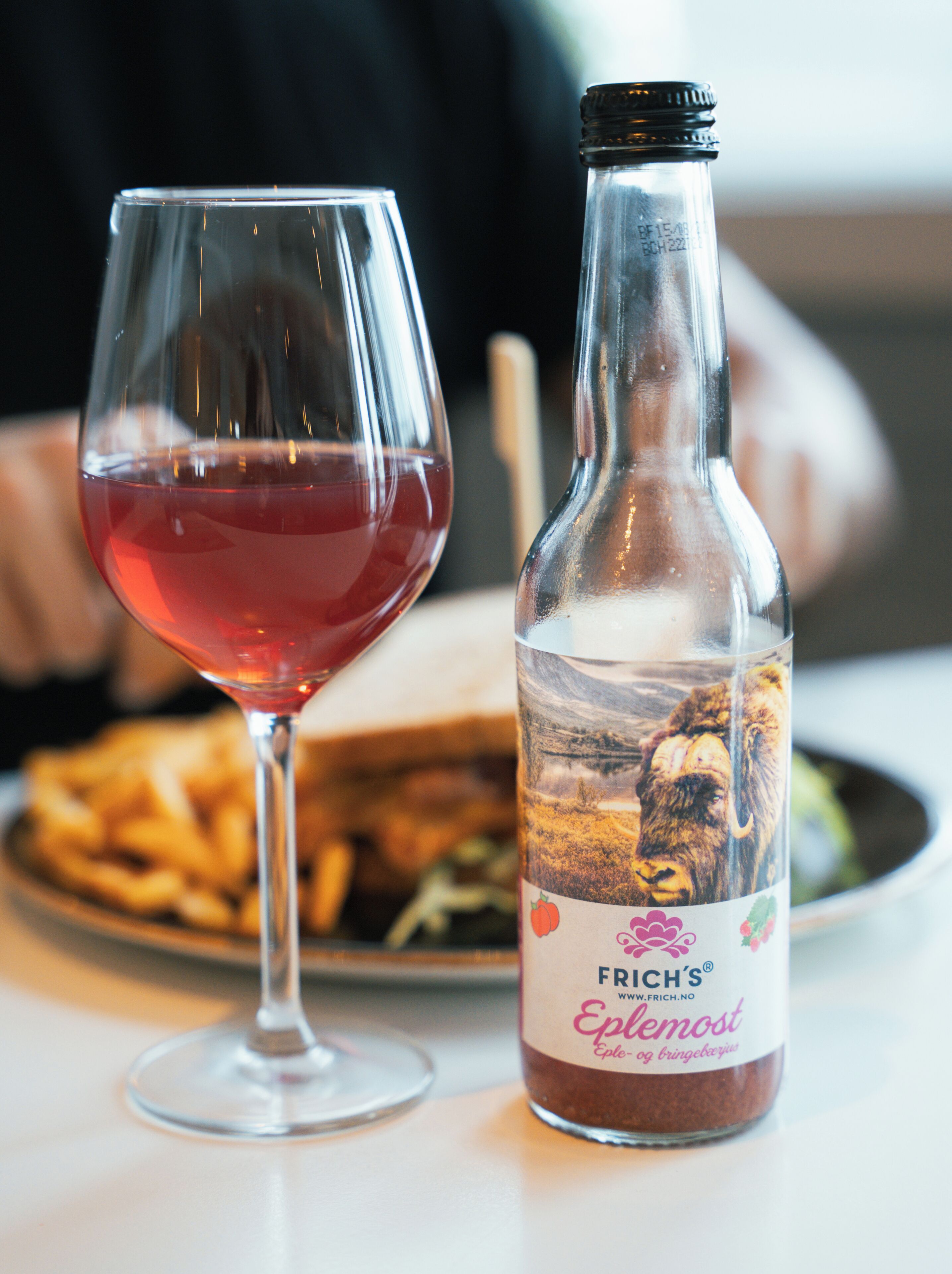 A bottle of Frich's Eplemost wine and a glass of red wine on a table.