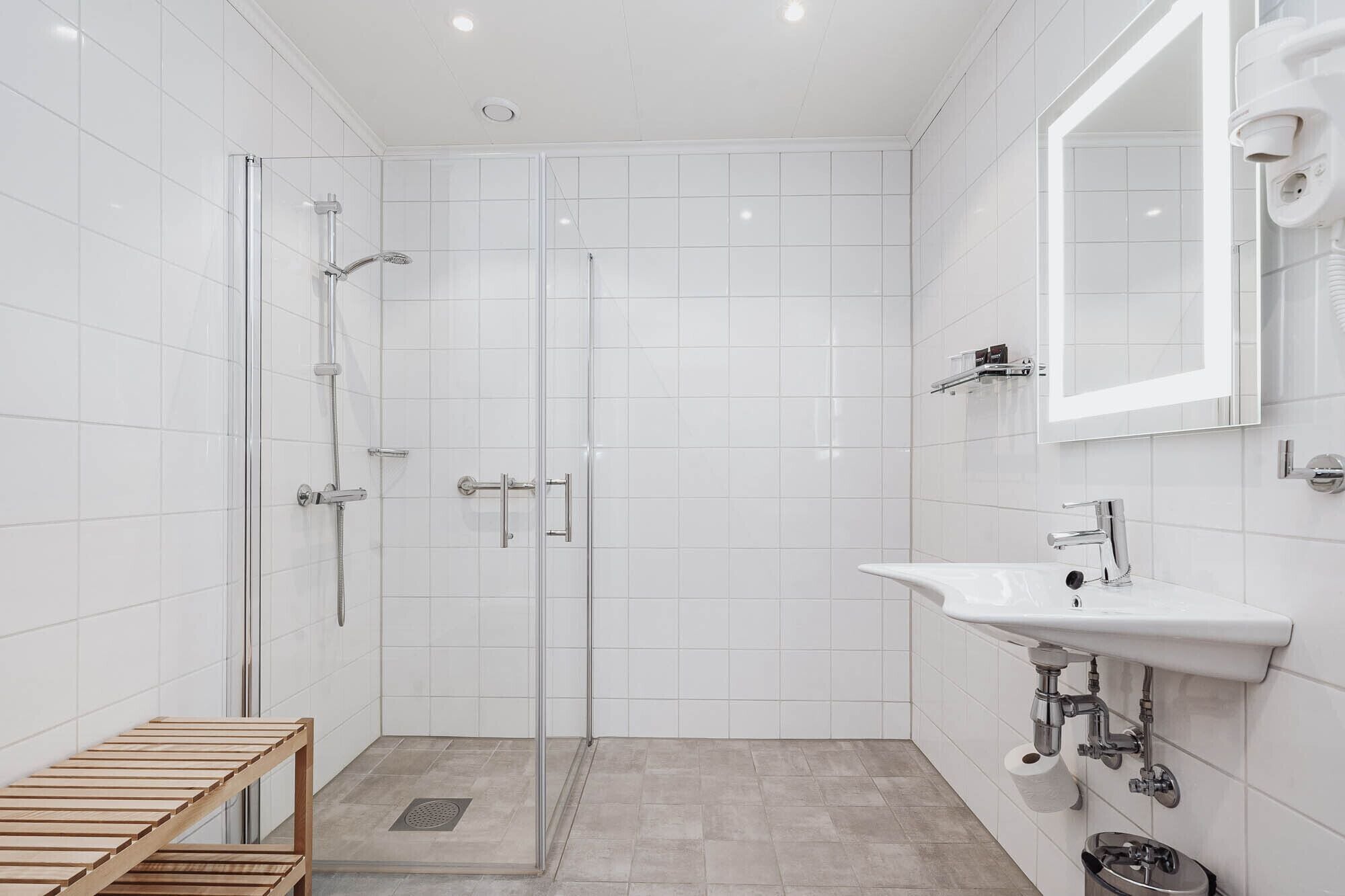 A modern bathroom with a glass shower enclosure, a sink with a mirror, and a wooden bench.