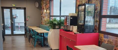 Un interior de restaurante con mesas y sillas de madera, un mostrador rojo y una pared decorada con carteles.