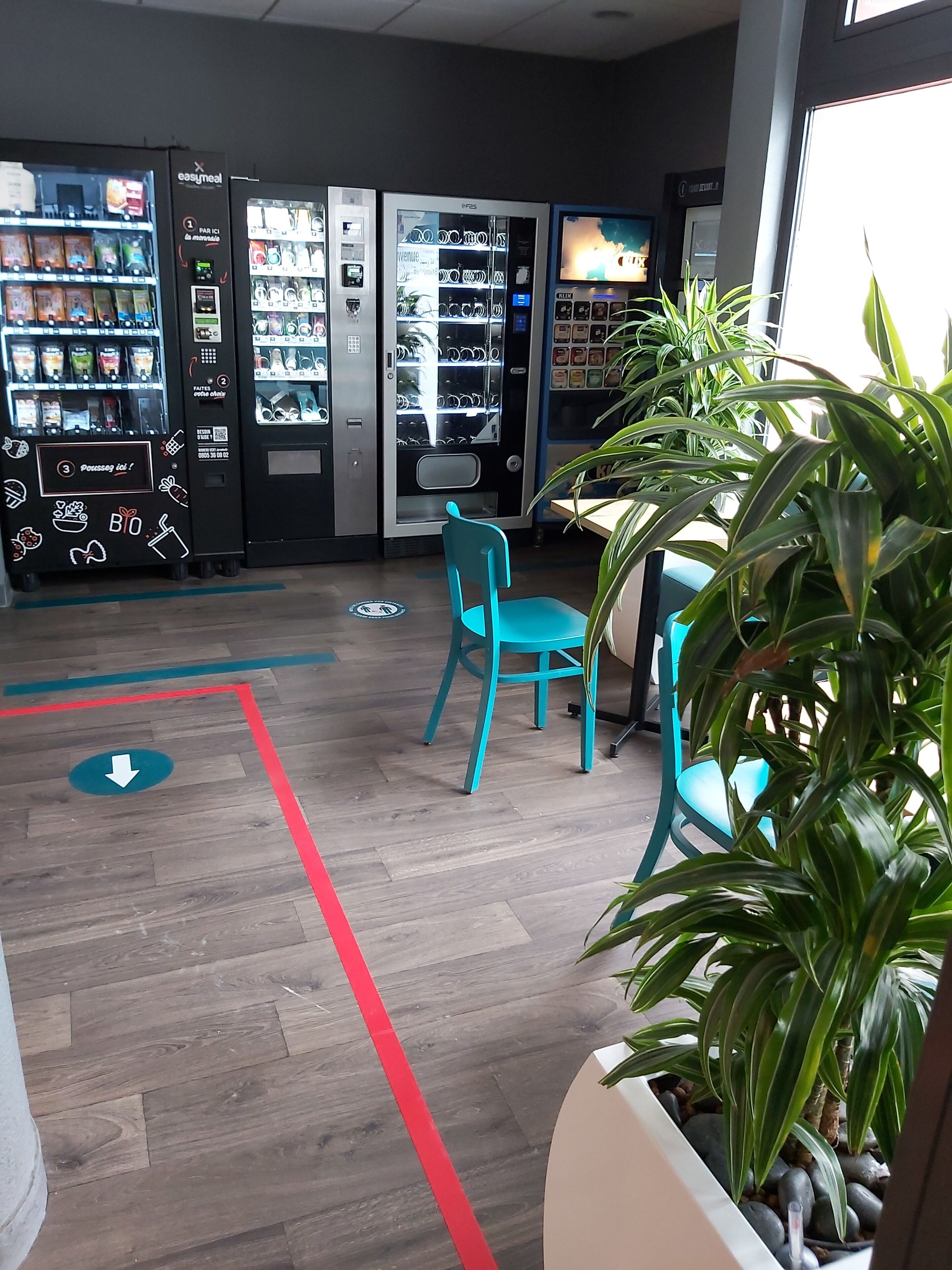 Een moderne binnenruimte met automaten, teal stoelen en potplanten.