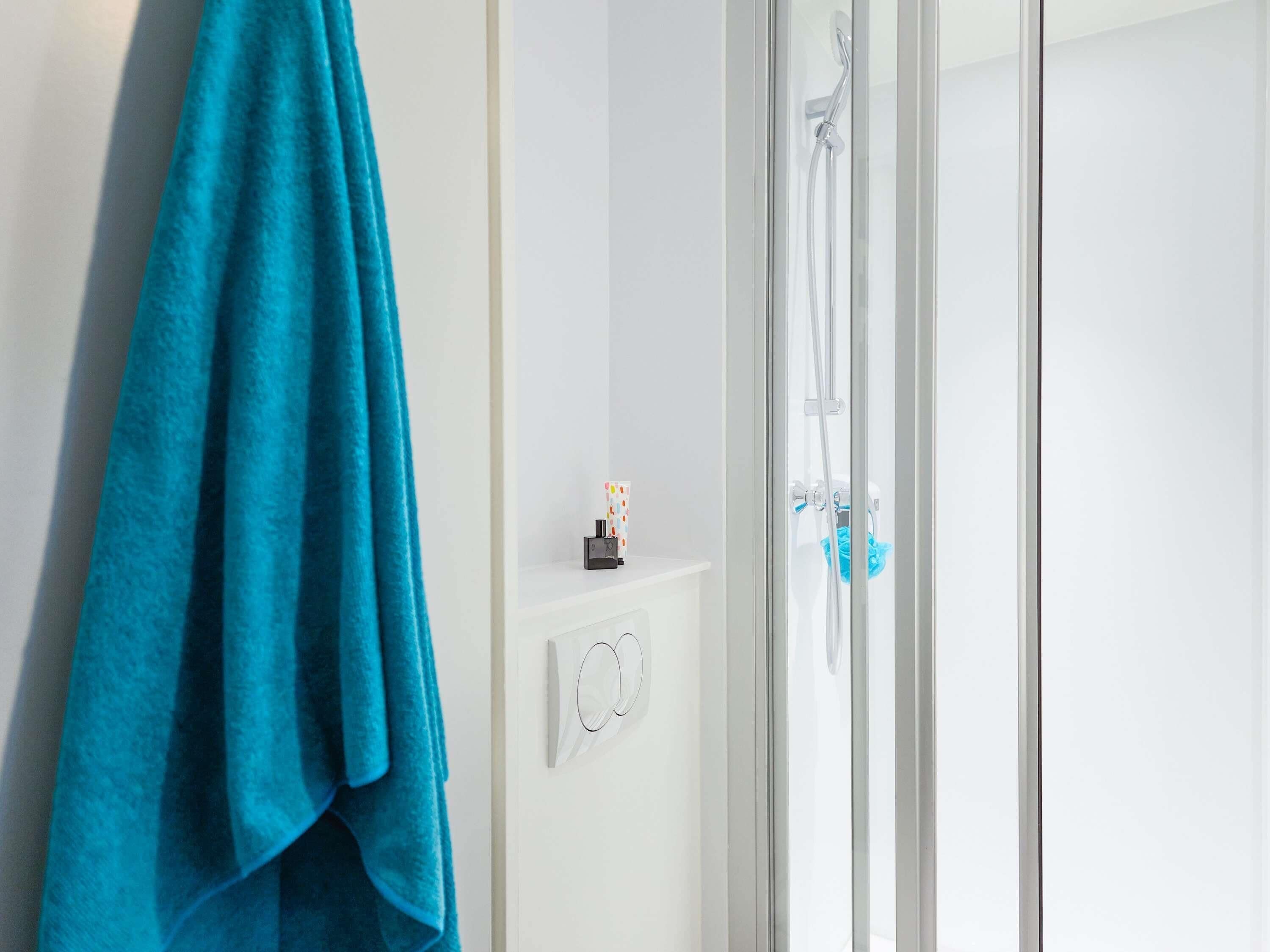 Ein Badezimmer mit Duschkabine aus Glas, einem Handtuchhalter mit blauem Handtuch und einer kleinen Ablage für Toilettenartikel.