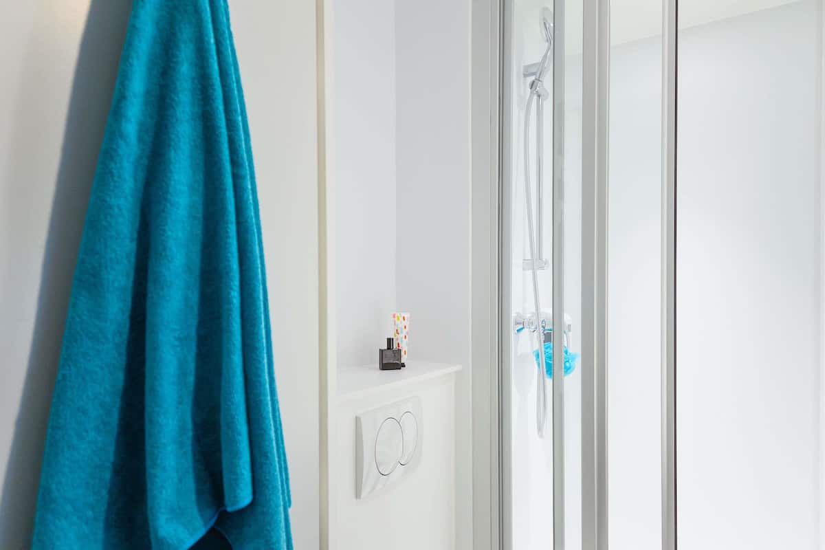 Ein Badezimmer mit Duschkabine aus Glas, einem Handtuchhalter mit blauem Handtuch und einer kleinen Ablage für Toilettenartikel.