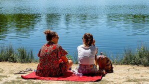 Two people sitting on a blanket by a lake with a boat in the background.