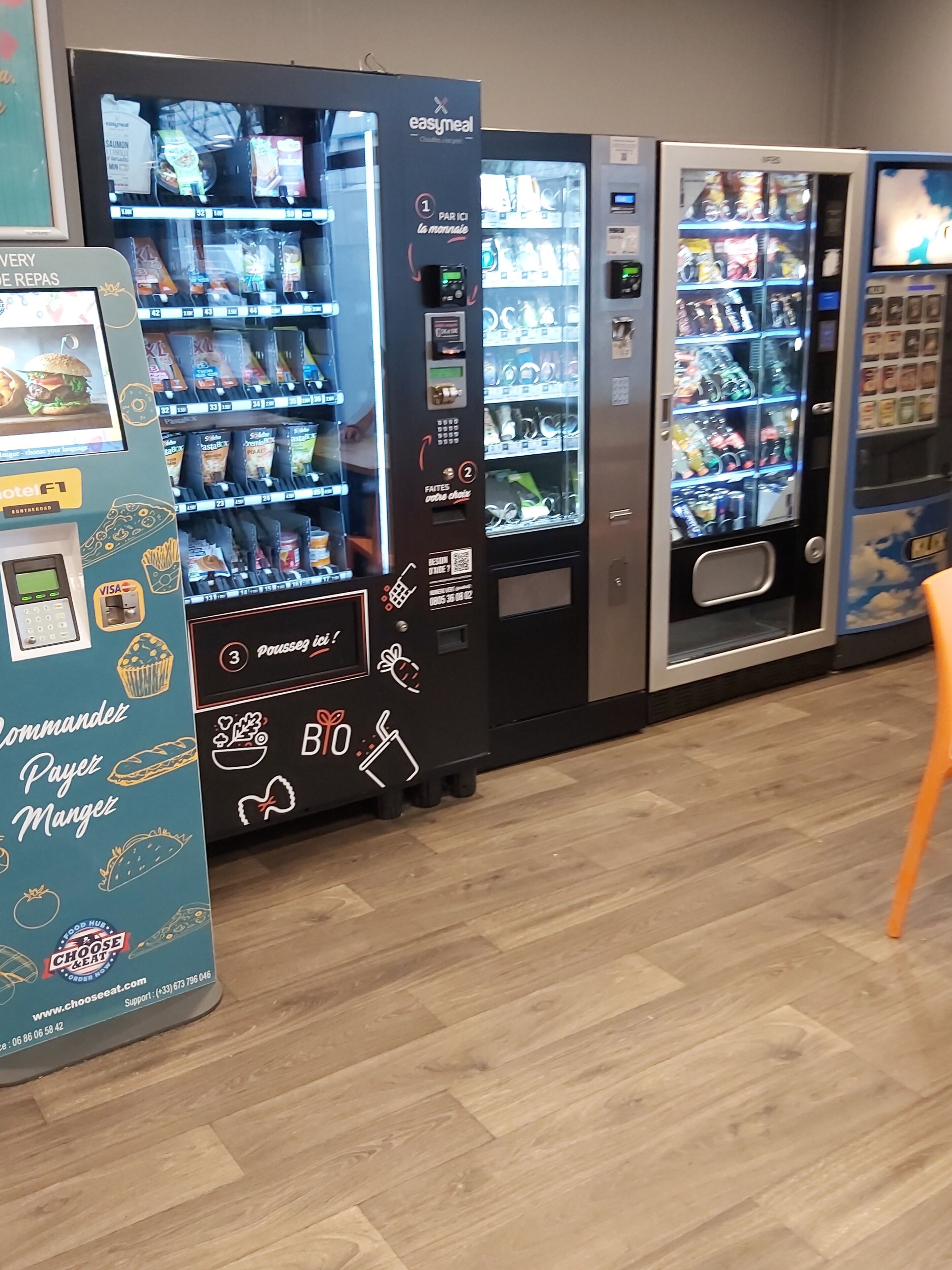 Een rij automaten met diverse opties voor eten en drinken, waaronder een automaat met een 'Payez Mangéz' bord.