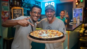 Una pizza sobre una tabla de madera sostenida por una persona.