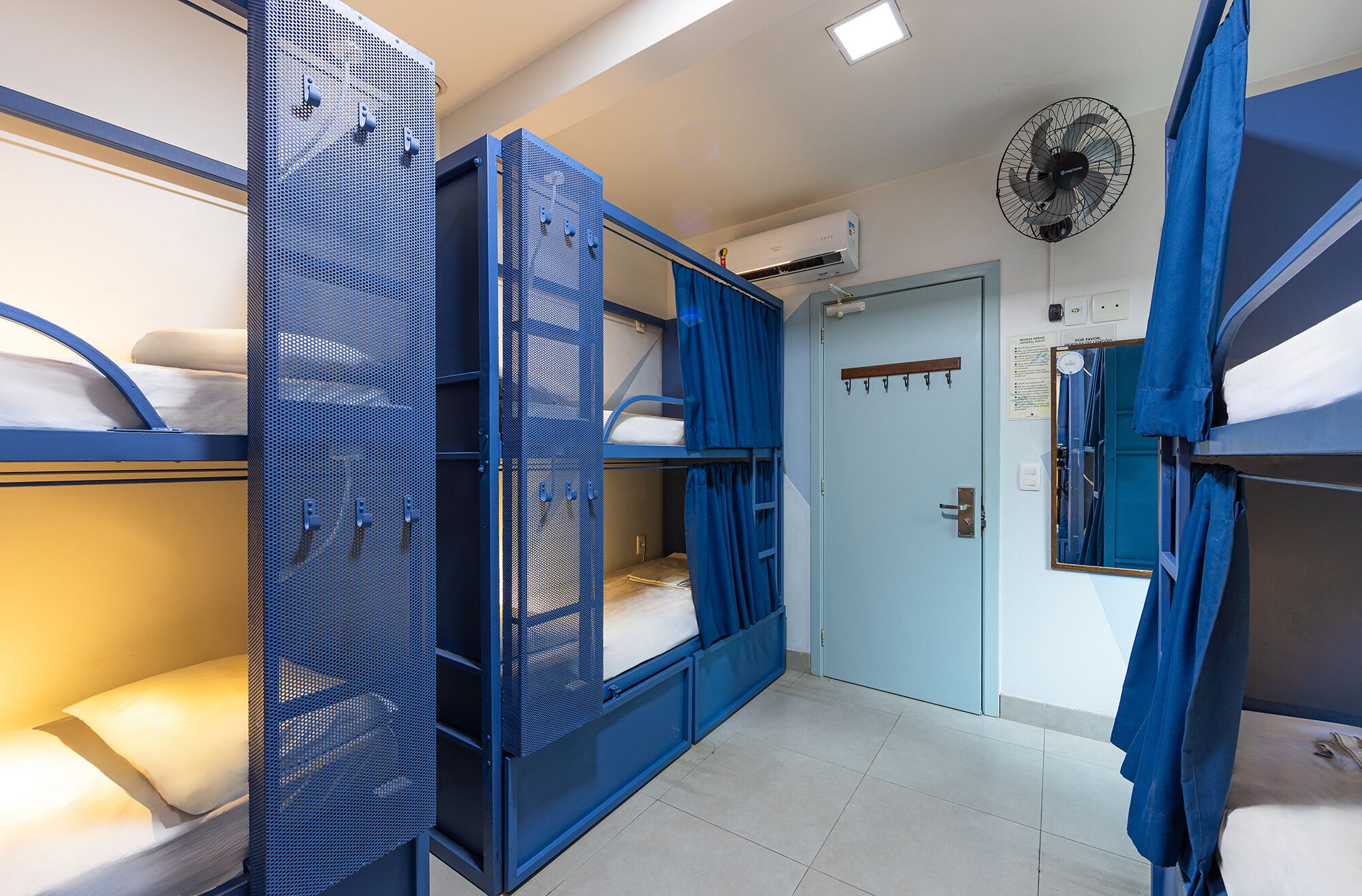 Habitación tipo dormitorio con literas, una puerta y un ventilador.