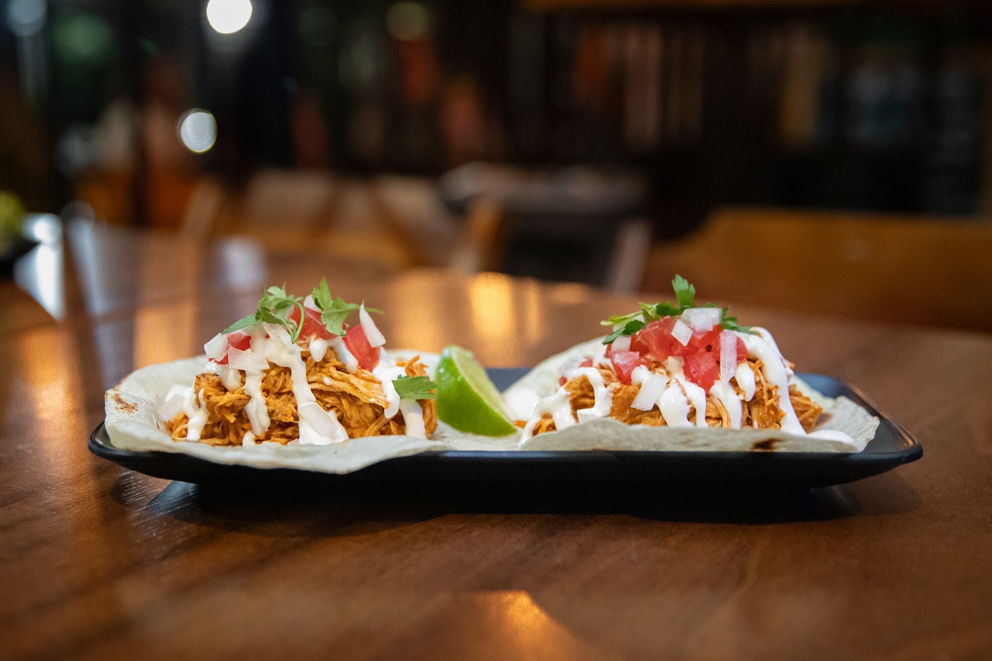 Dos tacos sobre un plato negro en una mesa de madera.