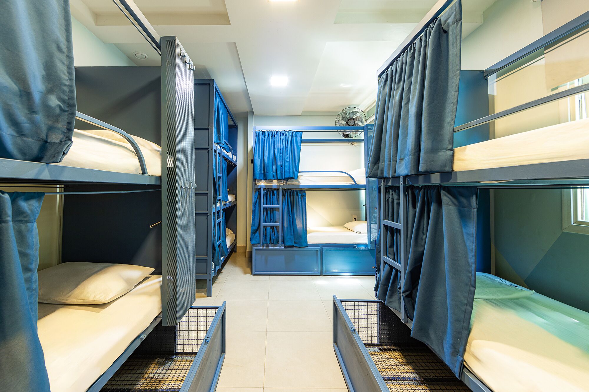 A train compartment with bunk beds, a fan, and curtains.