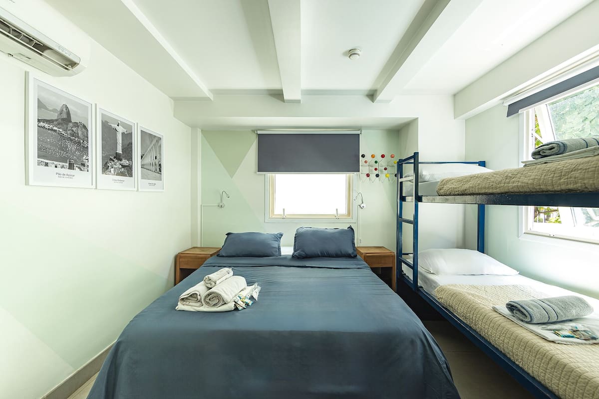 Quarto estilo dormitório com beliches, uma cama de solteiro e uma janela com vista.