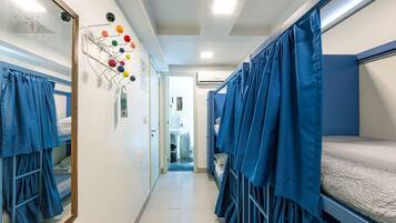 Un pasillo estrecho con literas a ambos lados, un tendedero de pared con bolas de colores, y un baño visible con lavamanos e inodoro.