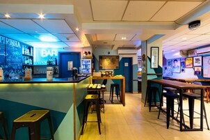 A bar area with a neon sign, shelves with bottles, and stools.