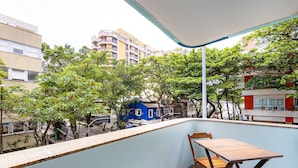 Un balcón con mesa y sillas de madera, con vista a un paisaje urbano con edificios y árboles.