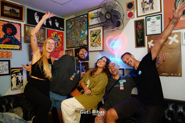 A group of people in a room with a neon heart sign, various framed pictures, and a fan on the wall. - El Misti Hostel Ipanema (Rio de Janeiro)