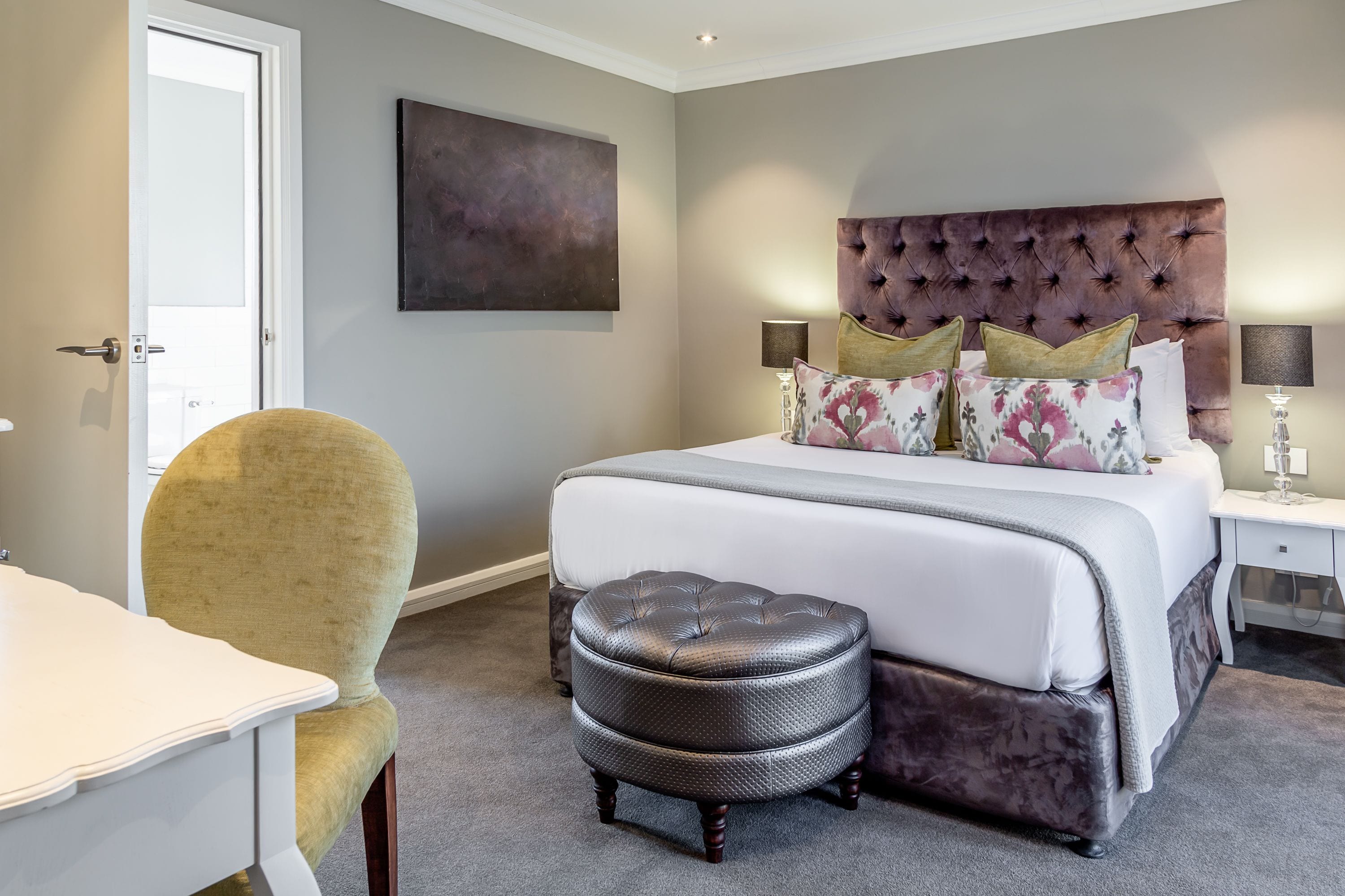 A bedroom with a tufted headboard, a large bed with multiple pillows, a bedside table with lamps, and a chair.