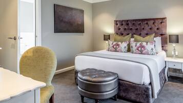 A bedroom with a tufted headboard, a large bed with multiple pillows, a bedside table with lamps, and a chair.