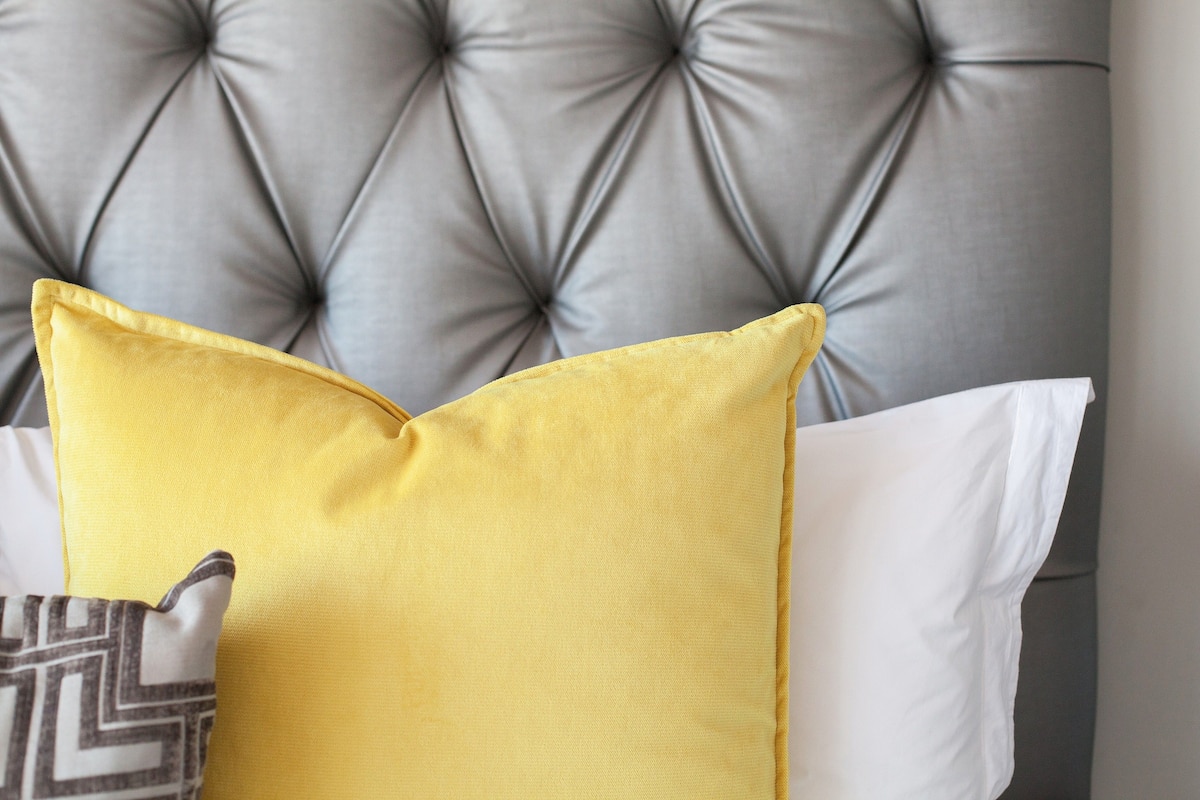 Une tête de lit grise, ornée de motifs en relief, avec un coussin jaune et un autre coussin à motifs.