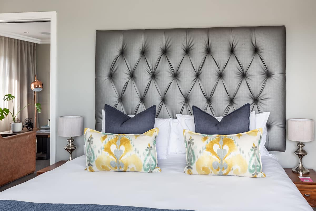 Un lit bien fait, avec une tête de lit capitonnée, deux coussins décoratifs et des lampes de chevet.