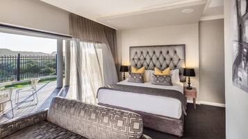 Habitación de hotel con una cama grande, un sofá, un balcón con vistas y un cabecero moderno.