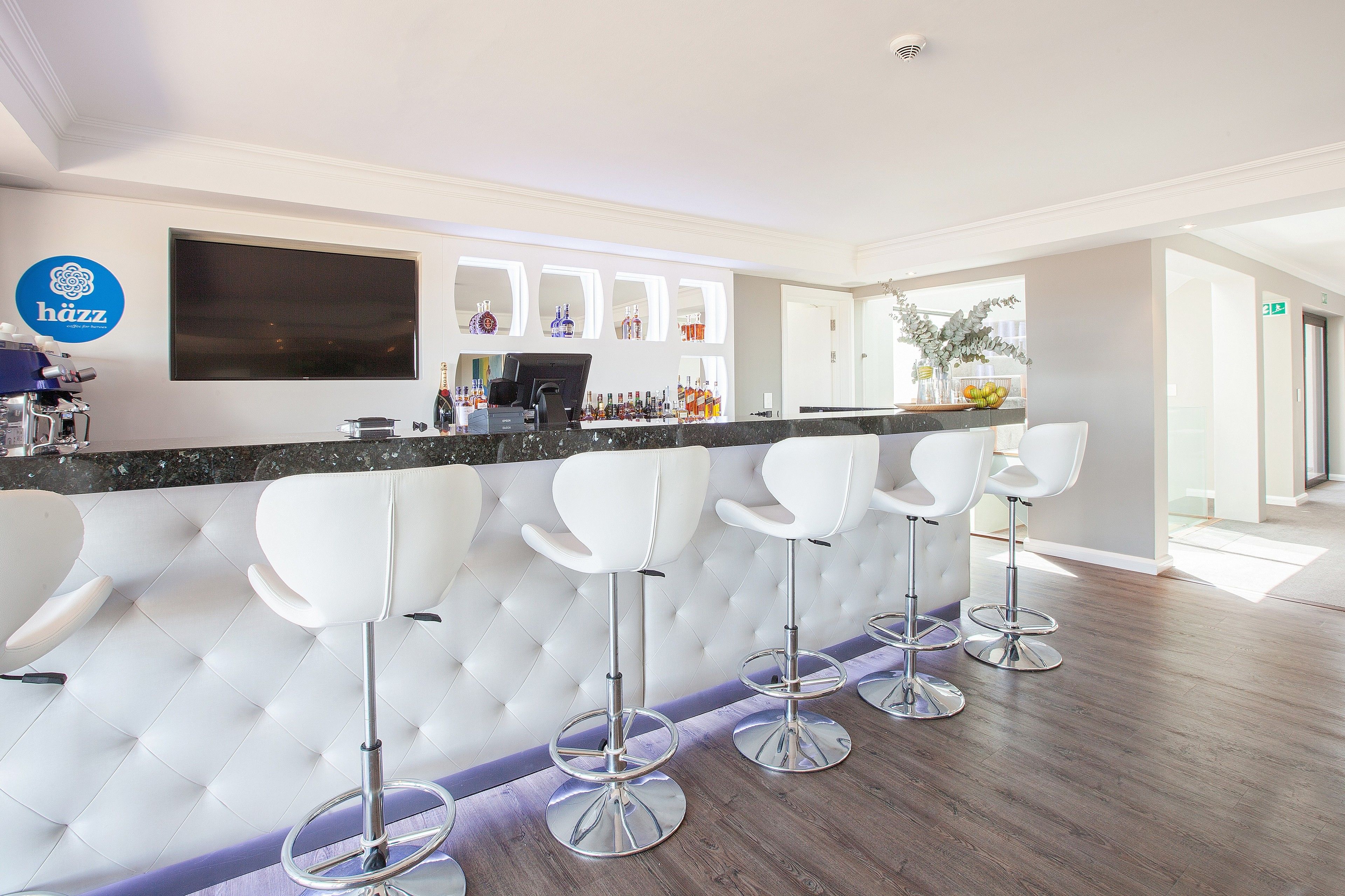 A bar area with a modern design, featuring a large flat-screen TV, a bar counter, and white bar stools.