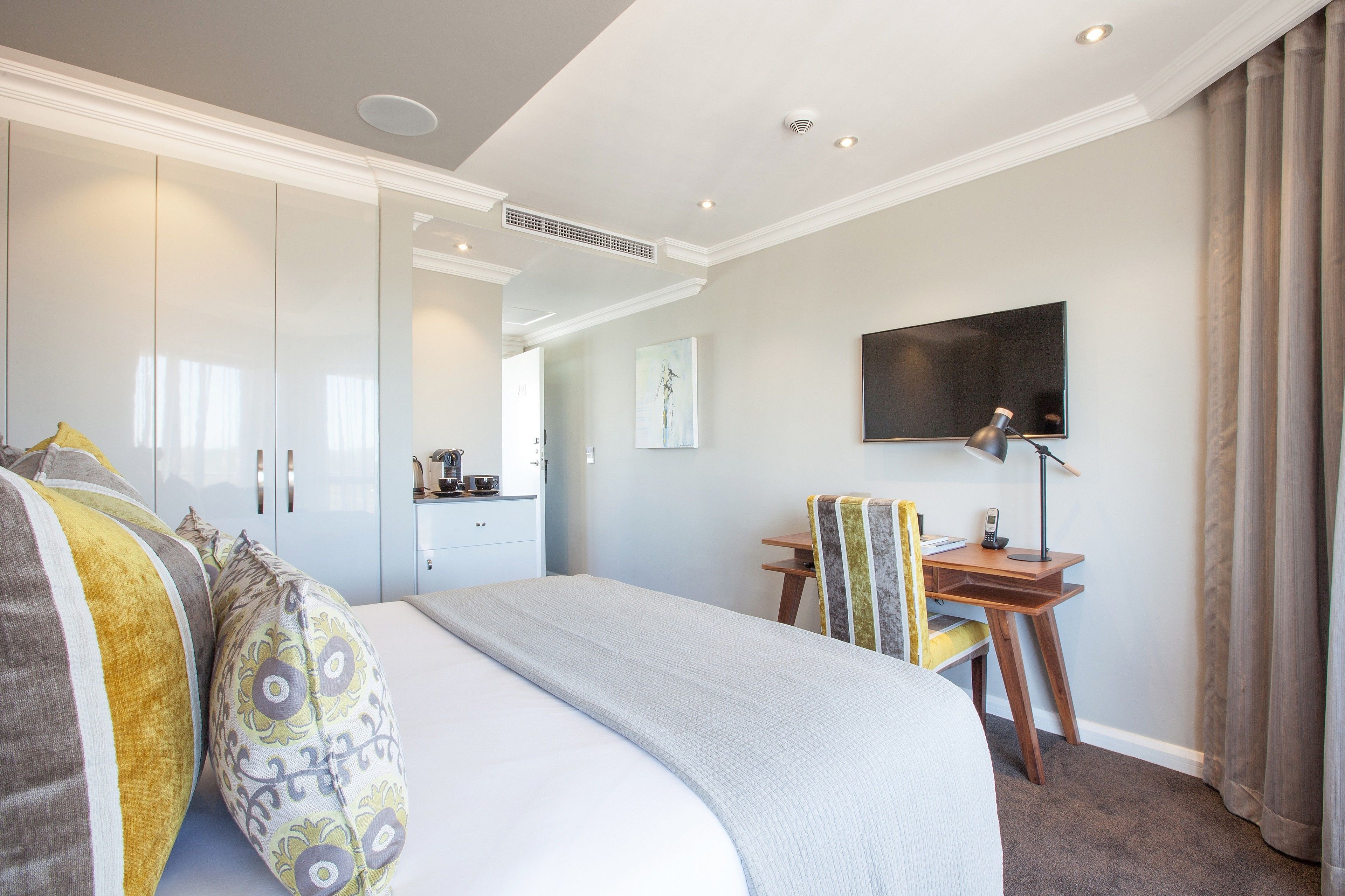 A hotel room with a large bed, a desk with a chair, a flat-screen TV, and a wardrobe.
