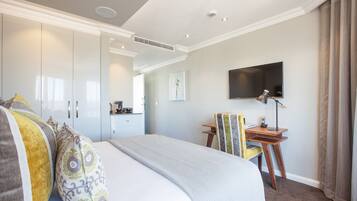 A hotel room with a large bed, a desk with a chair, a flat-screen TV, and a wardrobe.