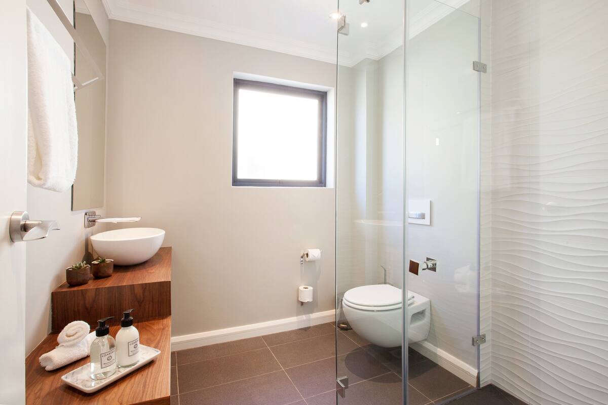 Une salle de bain moderne avec un grand lavabo blanc, une douche en verre et une petite fenêtre qui laisse entrer la lumière naturelle.