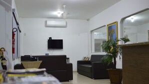Un'area reception con una TV a schermo piatto, due divani neri, una pianta in vaso e un bancone in legno.