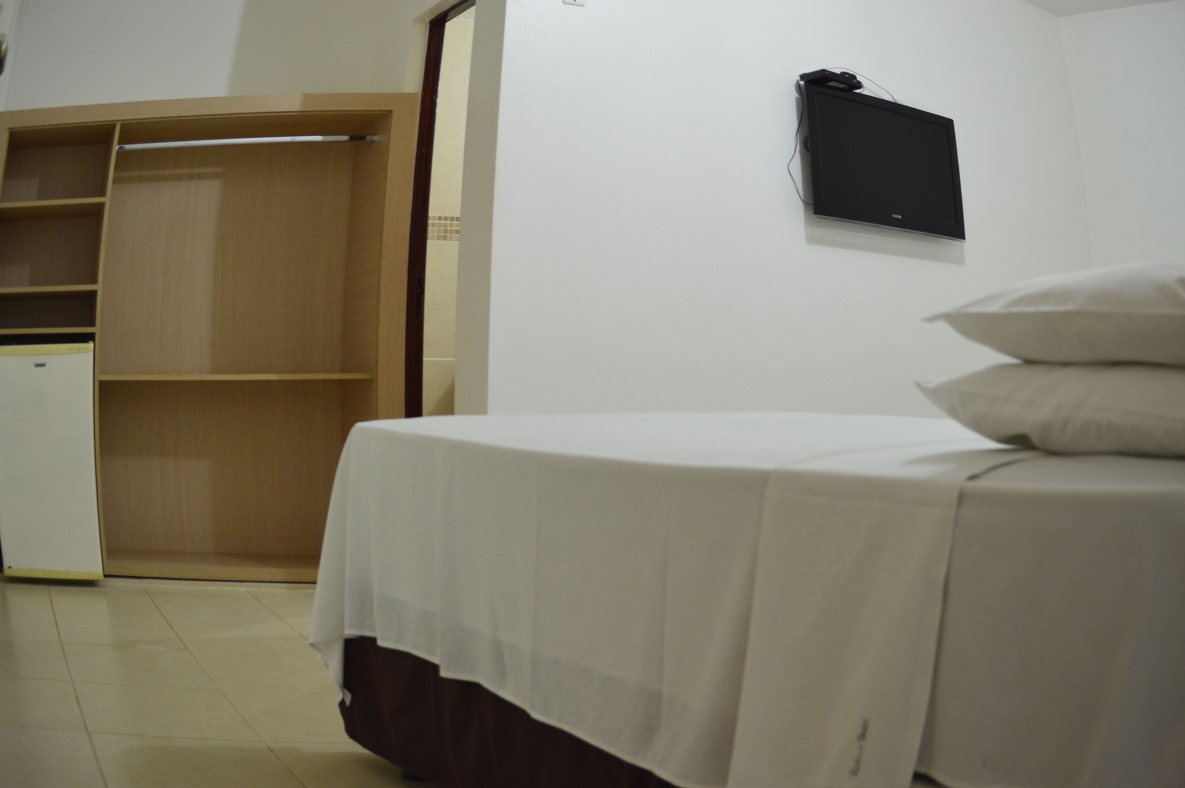 A bedroom with a bed, a wardrobe, and a flat-screen TV mounted on the wall.