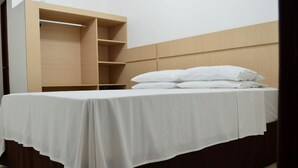 Un letto rifatto con lenzuola e cuscini bianchi, una testiera in legno e una libreria a sinistra.
