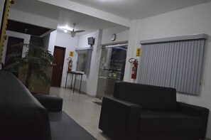 Um hall de entrada com balcão de recepção, relógio, extintor de incêndio e planta em vaso.