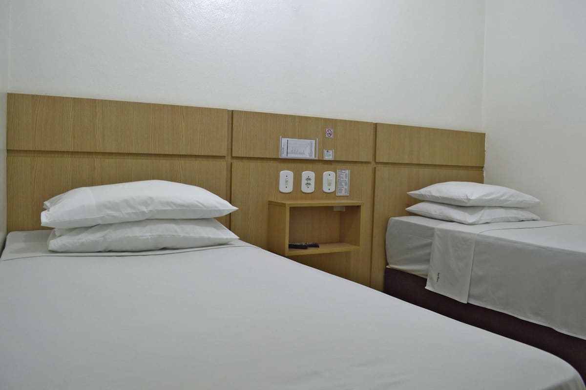 A hotel room with a wooden headboard, two beds with white linens, a wooden nightstand with a remote control, and a wall-mounted phone.