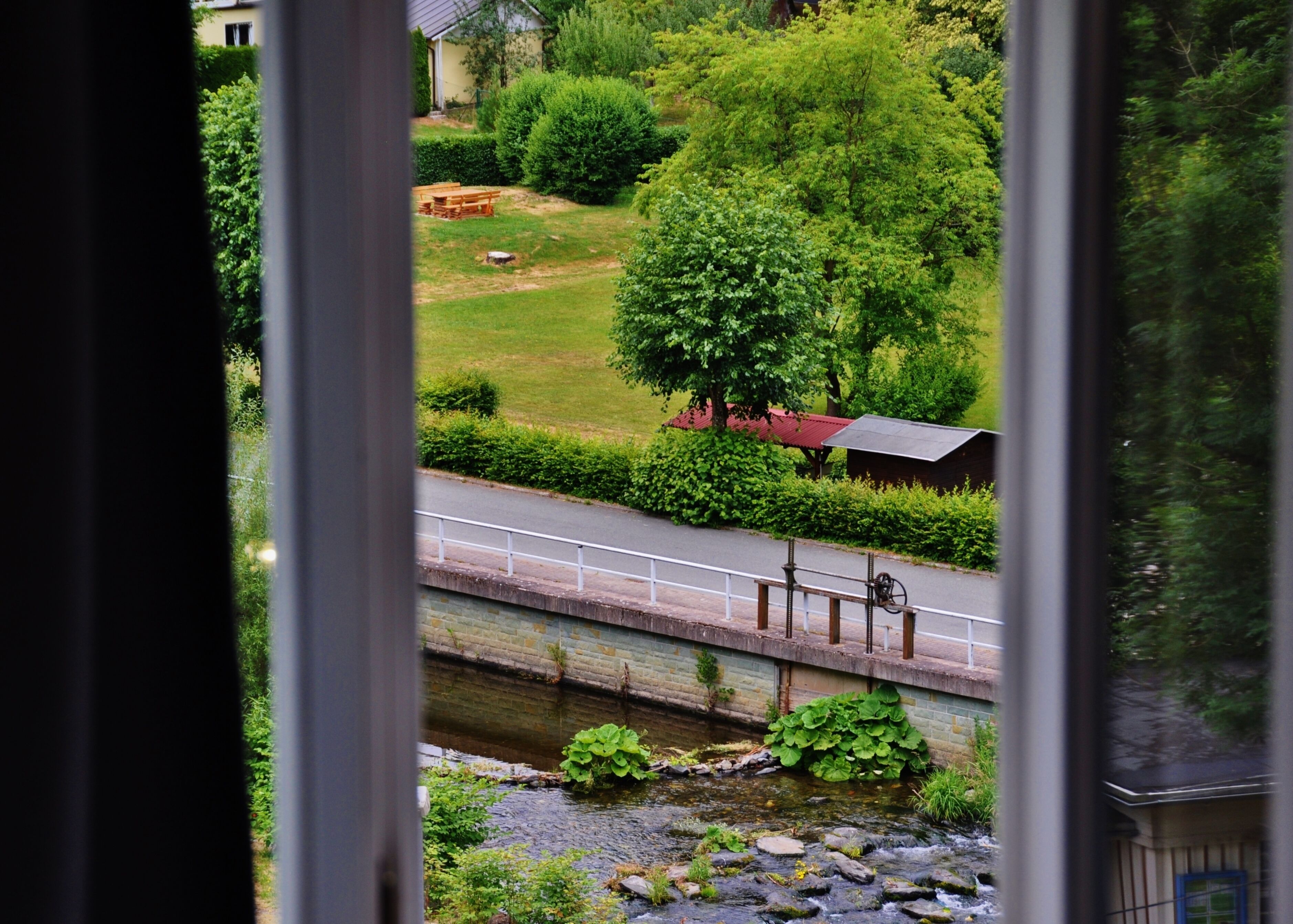 Vista de un jardín con un sendero, un estanque pequeño y un edificio con tejado rojo.