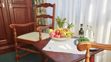 A wooden dining table with a white tablecloth, a wooden chair, a fruit bowl, and two bottles on the table.