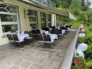 Een terras buiten met tafels en stoelen, een gebouw met grote ramen en een balkonhek met ballonnen.
