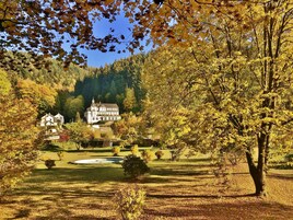 Uma grande propriedade com um edifício imponente, cercada por um jardim bem cuidado e um lago.