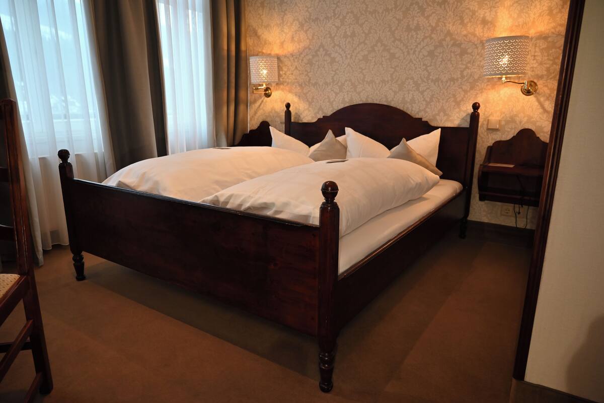 Un lit bien fait, avec du linge de lit blanc, une tête de lit en bois et deux lampes fixées au mur.