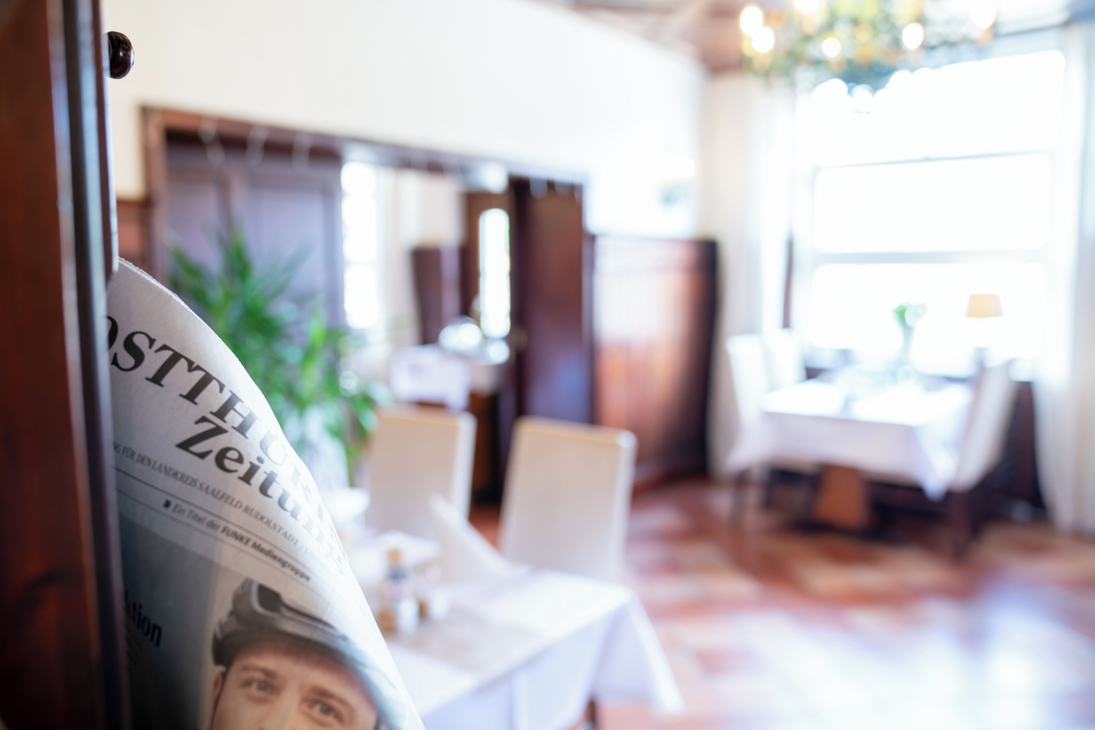 Un periódico con un titular visible, un comedor con mesas y sillas, y una planta al fondo.