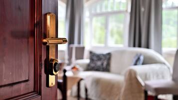 Eine Holztür mit Messinggriffen, ein weißes Sofa mit einem gemusterten Überwurf und ein Fenster mit Vorhängen in einem Zimmer.
