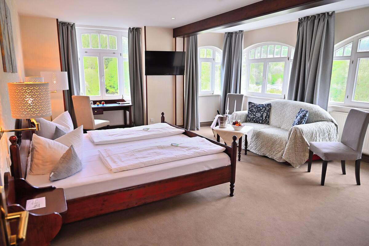 Une chambre d’hôtel équipée d’un lit, d’un bureau, d’une télévision, d’un canapé et de grandes fenêtres.