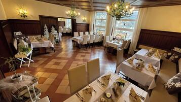 A dining area with multiple tables set for a meal, featuring white tablecloths and neatly arranged cutlery.