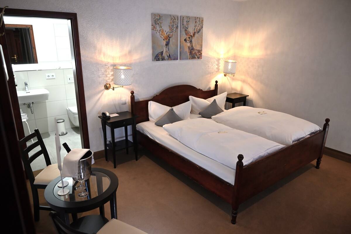 Une chambre à coucher avec un lit double, des tables de chevet, une petite table de nuit, une chaise et une table sur laquelle se trouvent un verre et une carafe.