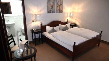 Un dormitorio con una cama doble, mesitas de noche, una silla y una mesa con un vaso y una jarrón.