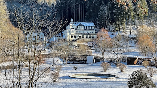 A large, multi-story building with a symmetrical facade, surrounded by snow-covered grounds and trees. - Flair Hotel Waldfrieden (Schwarzatal)