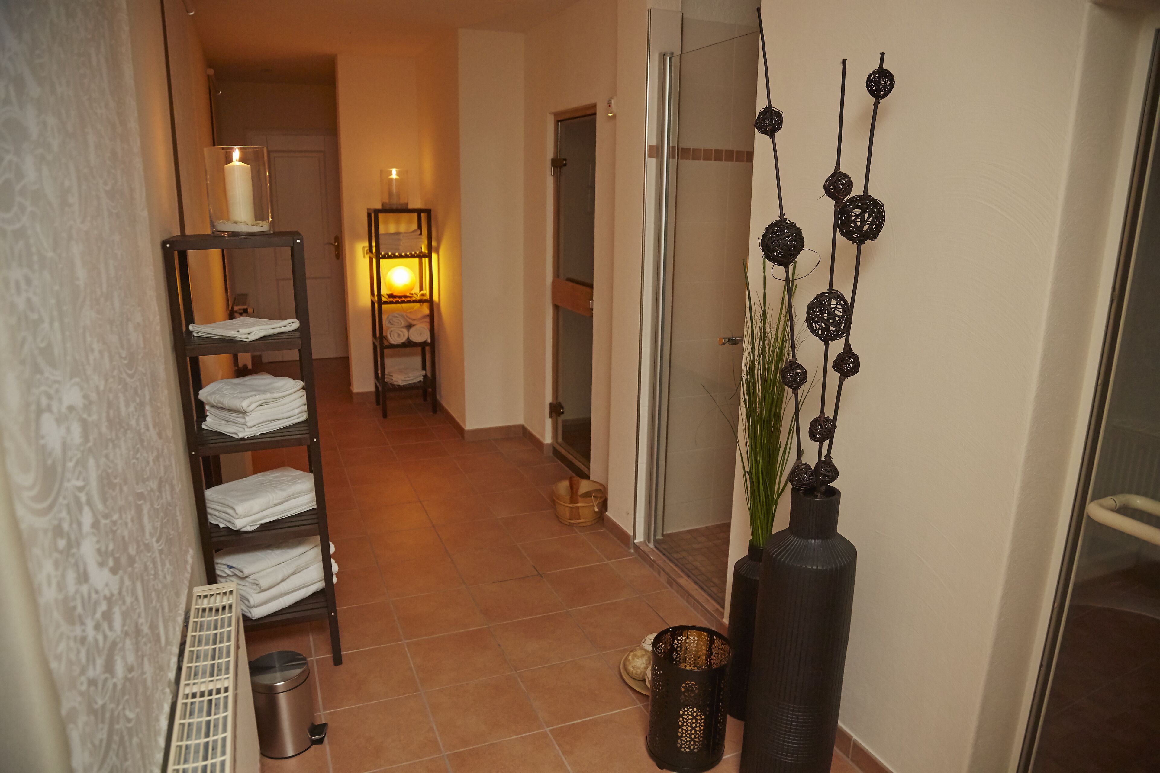 A hallway with a towel rack, a lit lamp, a trash bin, and a decorative vase.