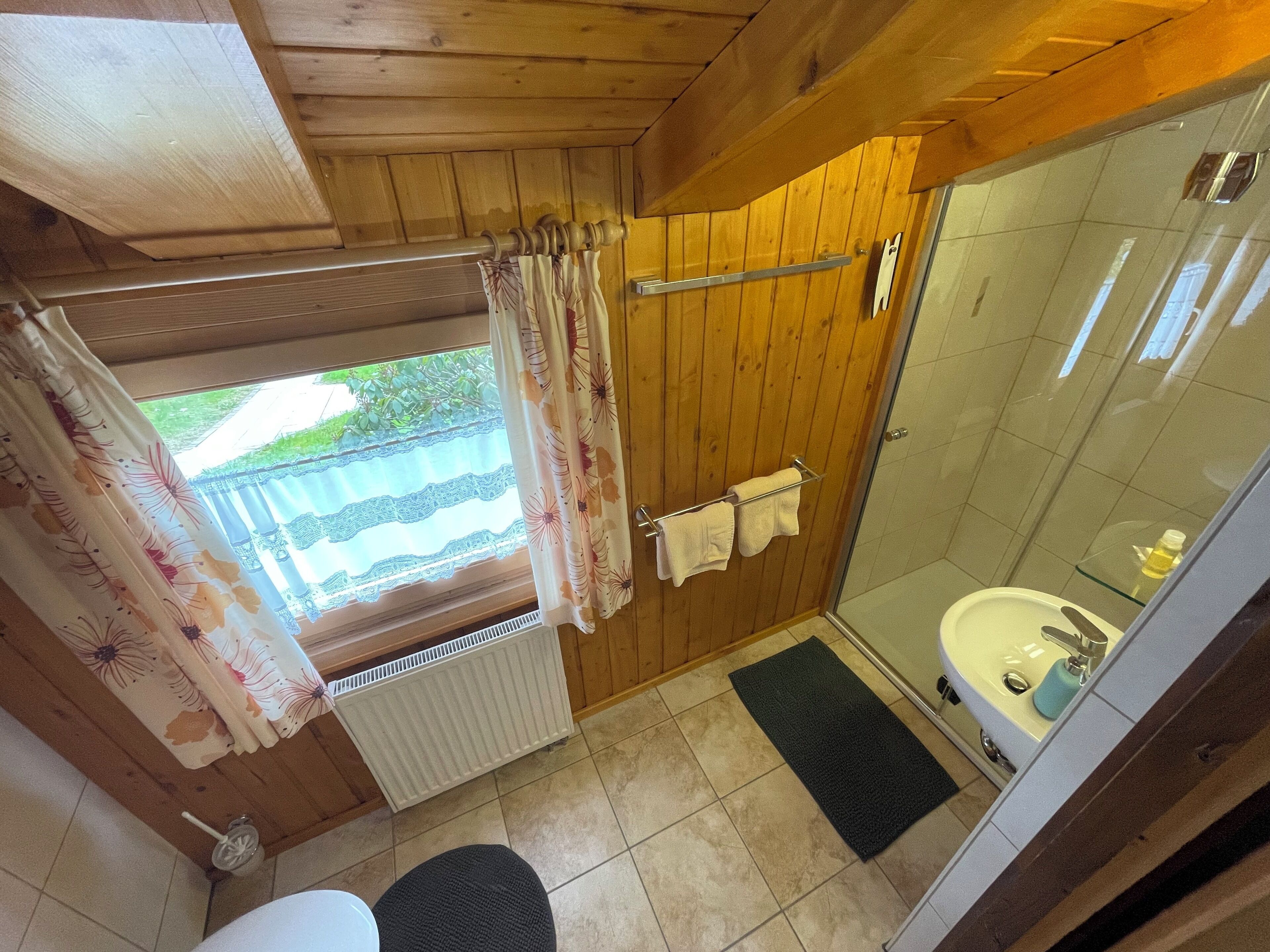 Une salle de bain aux murs lambrissés, dotée d’une douche en verre, de toilettes et d’un radiateur.