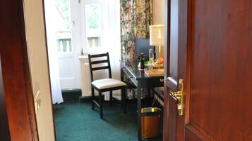 Una habitación con puerta de madera con el número 19, un escritorio con lámpara, una silla y una ventana con cortinas.