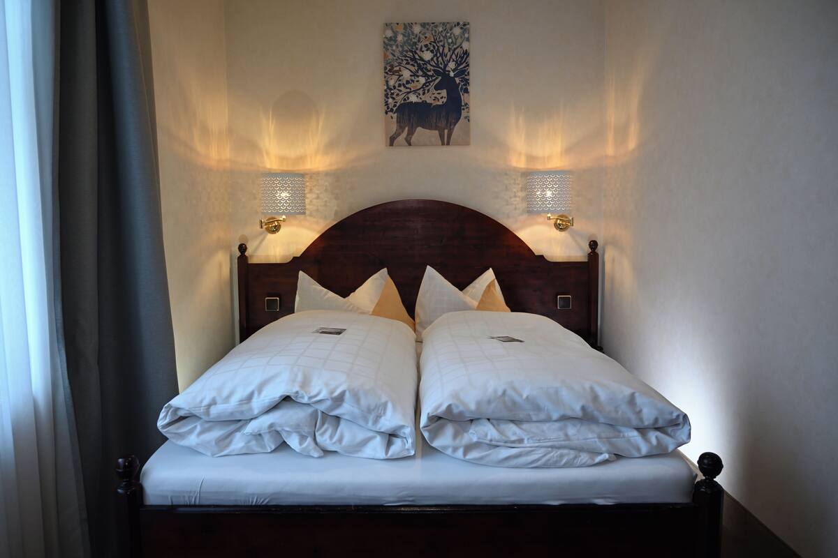 Un lit bien fait, avec deux oreillers, une tête de lit ornée d’un motif décoratif et des appliques murales.