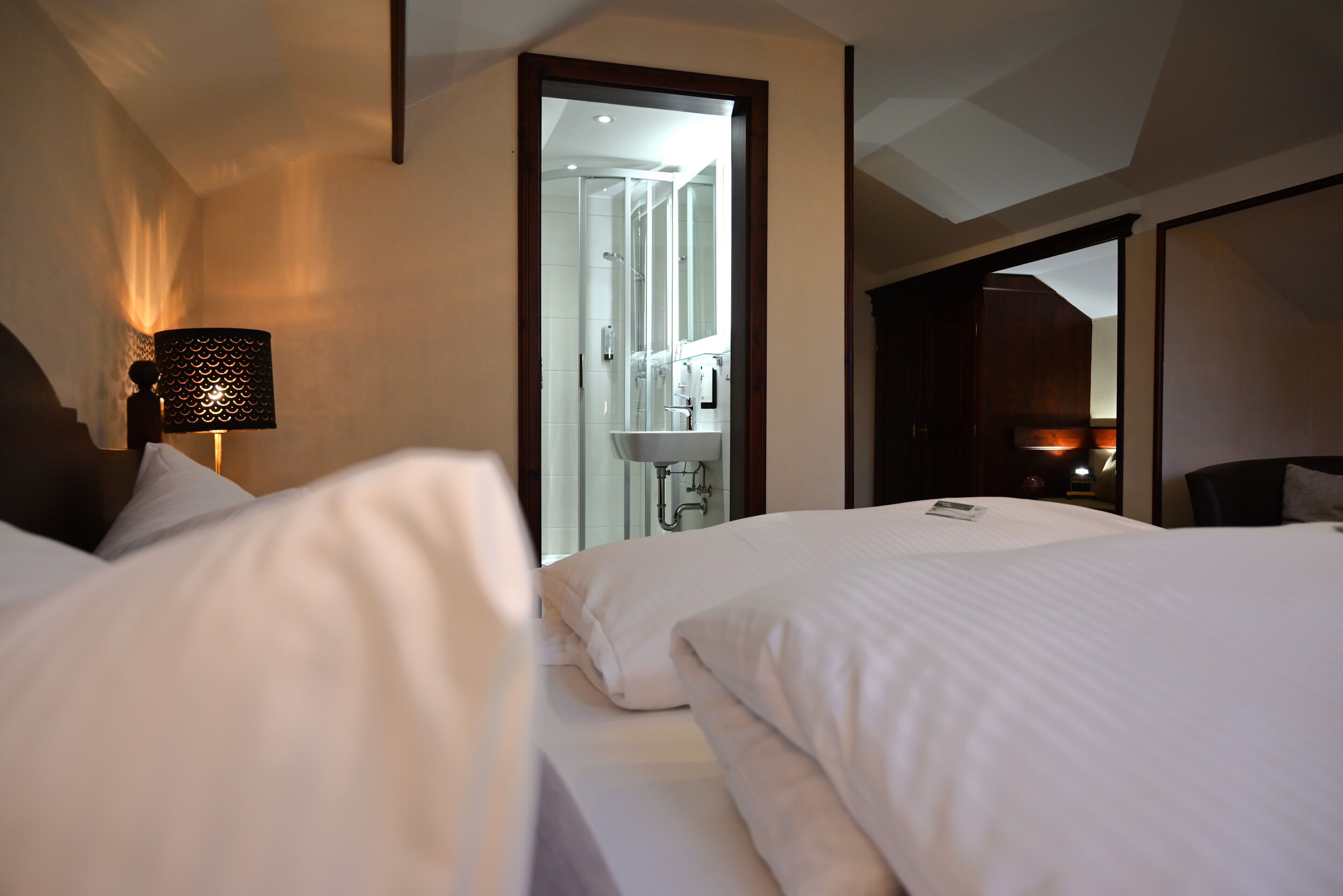 Una habitación de hotel con una cama, una lámpara, un baño visible a través de un umbral y una mesita de noche.