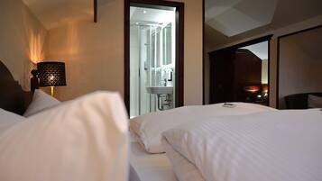 Una habitación de hotel con una cama, una lámpara, un baño visible a través de un umbral y una mesita de noche.
